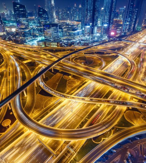Aerial view of big highway interchange with traffic in Dubai, UAE, at night. Scenic cityscape. Colorful transportation, communications and driving background.